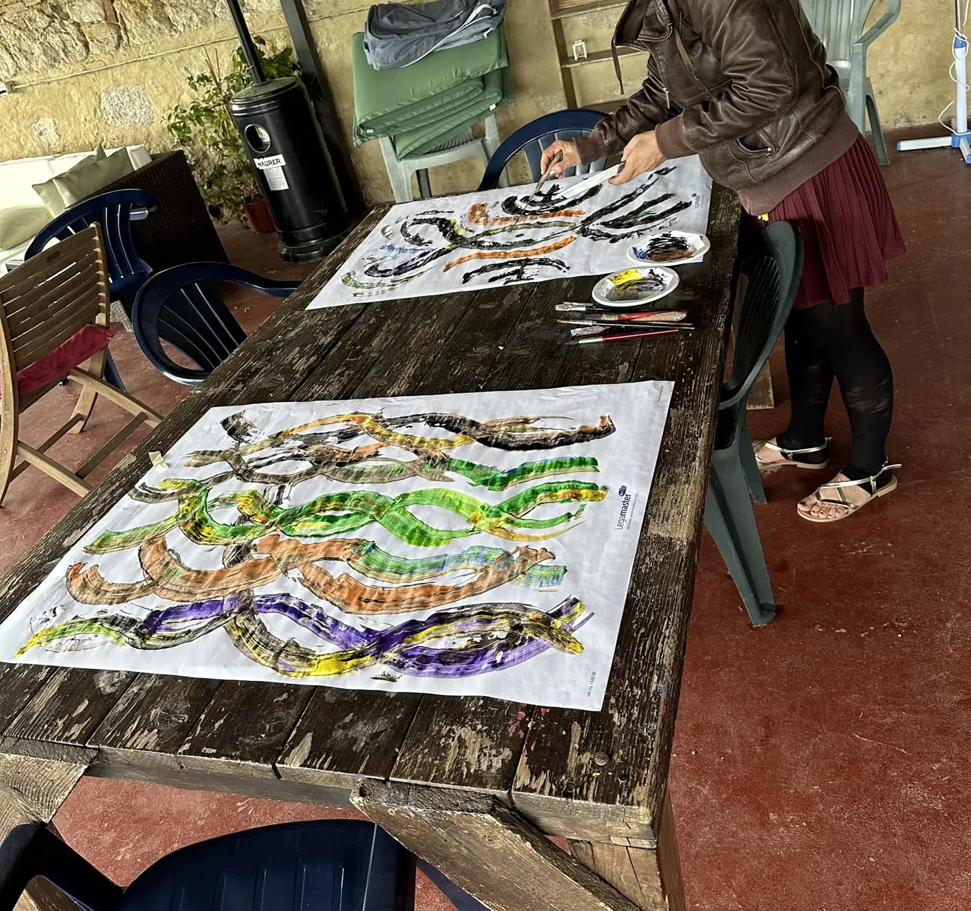 Un grande tavolo con disegni a colori su fogli, e una persona al lavoro